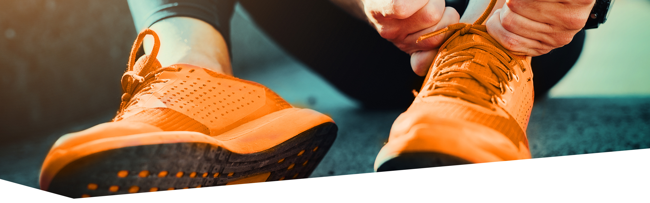 Sportler schnürt sich orange Turnschuhe zu, dabei sind nur die Füße und Hände zu sehen