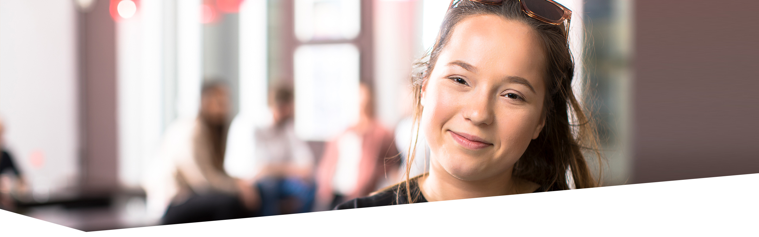 Junge Frau in der Ausbildung, die Betrachter anlächelt, weitere junge Menschen in der Ausbildung sprechen im Hintergrund miteinander