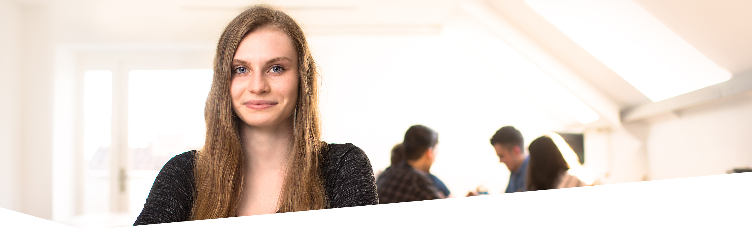 Schülerin der Dr. Buhmann Schule und Akademie, die den Betrachter anlächelt, weitere Schüler sprechen im Hintergrund miteiander