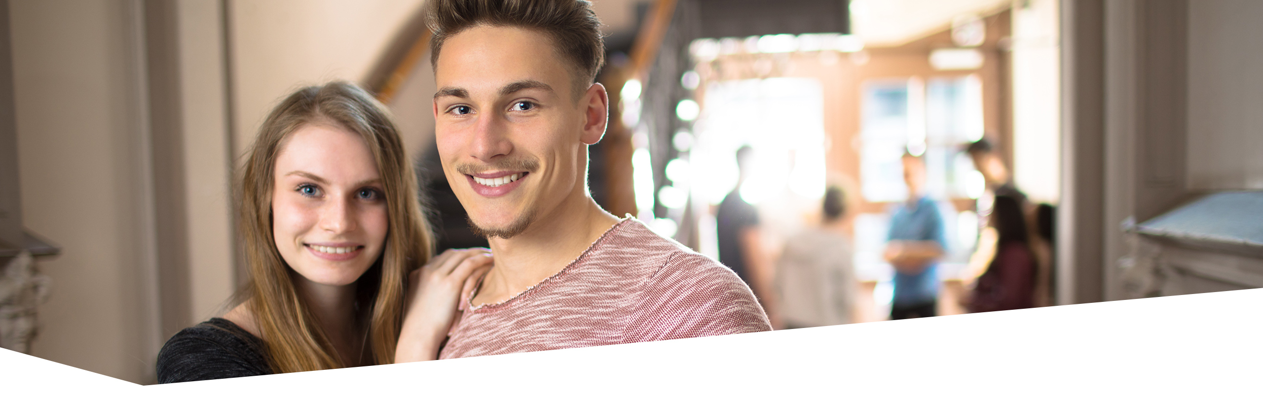 Gesicht von Berufstätiger und Berufstätigem, die Betrachter anlächeln, vier Schüler sprechen im Hintergrund miteinander