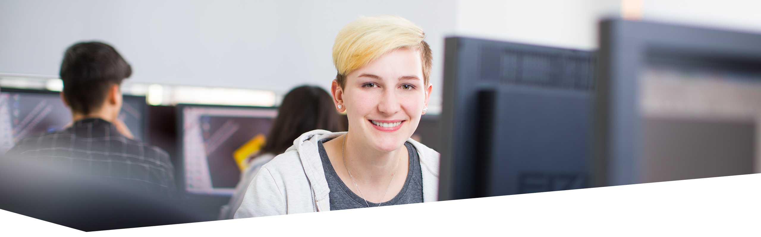 Bild von junger Frau in Ausbildung zur Gestaltungstechnischen Assistentin am Computer, zwei weitere Auszubildende an Computern im Hintergrund